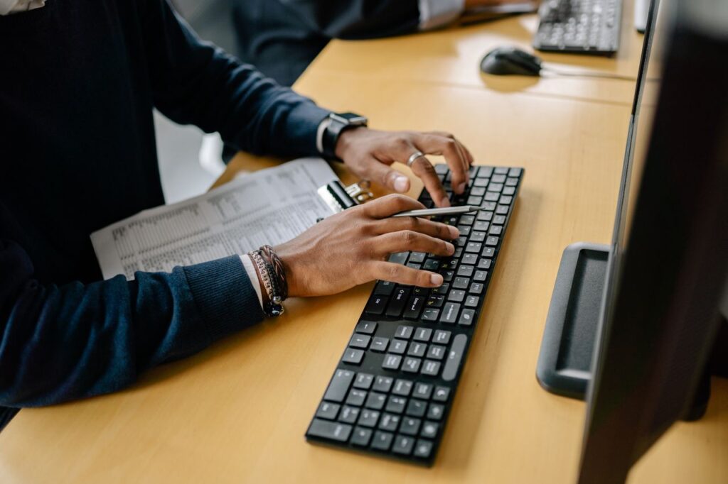 Close-up of hands typing on a keyboard in an office setting with clipboard nearby.